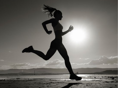 Low angle of a woman jogging down a beach in black and white